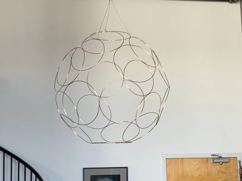 a slowly rotating hanging sculpture made of circular metal rings arranged in a dodecahedral pattern